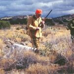 Bird hunter approaching a white bird dog on point in Arizona bird country.