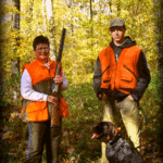 A bird hunter and guide with a dog and autumn, yellow woods in the background.