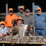 Six hunters and two gun dogs posing with harvested bobwhite quail.