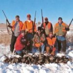 Large group of pheasant hunters posing behind their harvested birds.