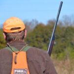 Close up looking over the should of a bird hunter in a brushy field. 