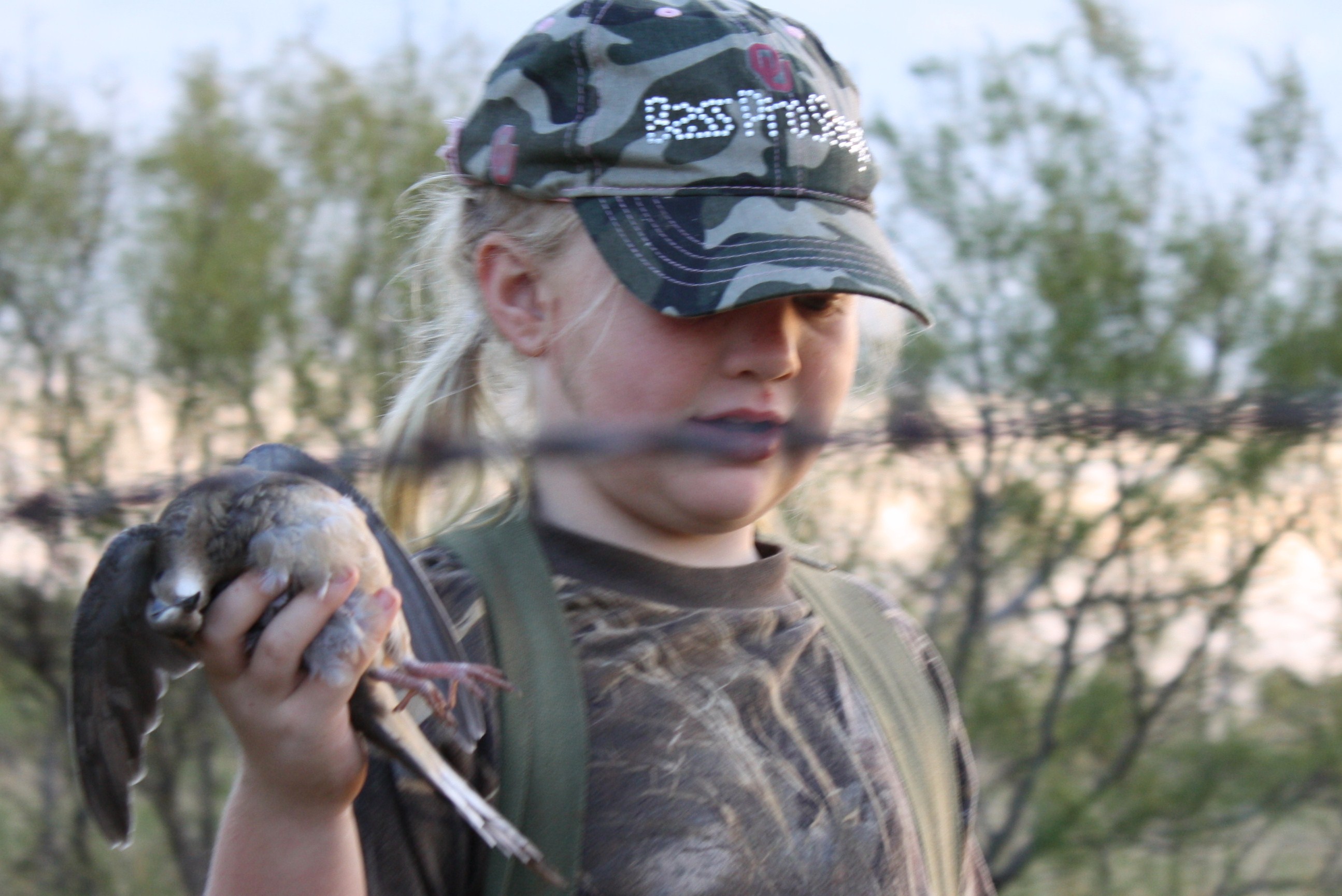 Young girl dressed in camo holding a harvested mourning dove.