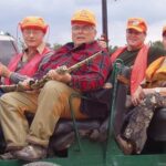 Several bird hunters being transported in a green hunting rig.