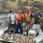 Four bird hunters and a bird dog on a boat posing behind a large number of harvested chukar.