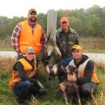 Four smiling bird hunters posing with their harvest game birds and gun dog.