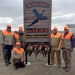 Five bird hunters posing in front of the outfitter's sign where their harvest of pheasants are displayed.