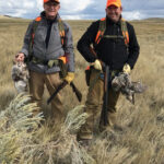 Two successful bird hunters carrying harvested game birds in from the field.