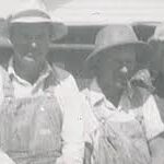 Old-fashioned black and white photo of two men in overalls.