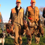 Hunters carrying many pheasants.