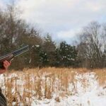 Hunter taking aim at a game bird in snowy field. 