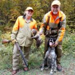 Two bird hunters with a gun dog showing off harvested ruffed grouse.