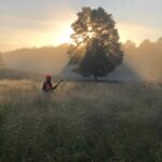 Landscape scene with filtered light and bird hunter wading through waist high grass.